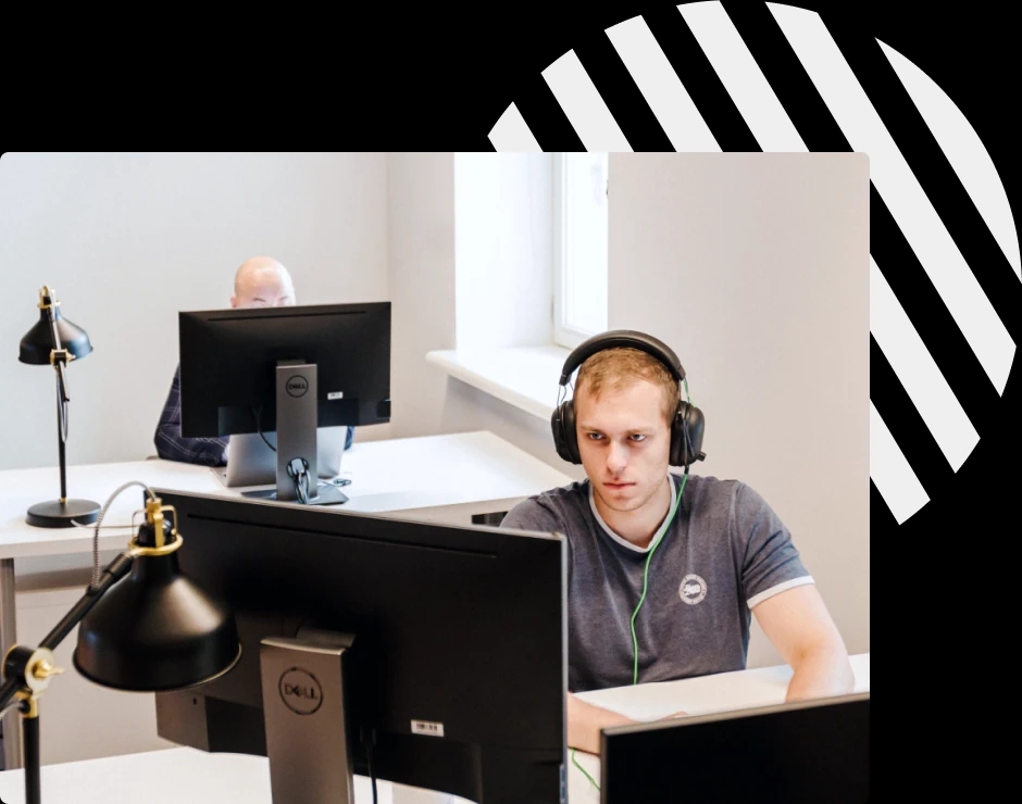 To personer som jobber ved skrivebord med store skjermer, en av dem bruker hodetelefoner og fokuserer på skjermen.